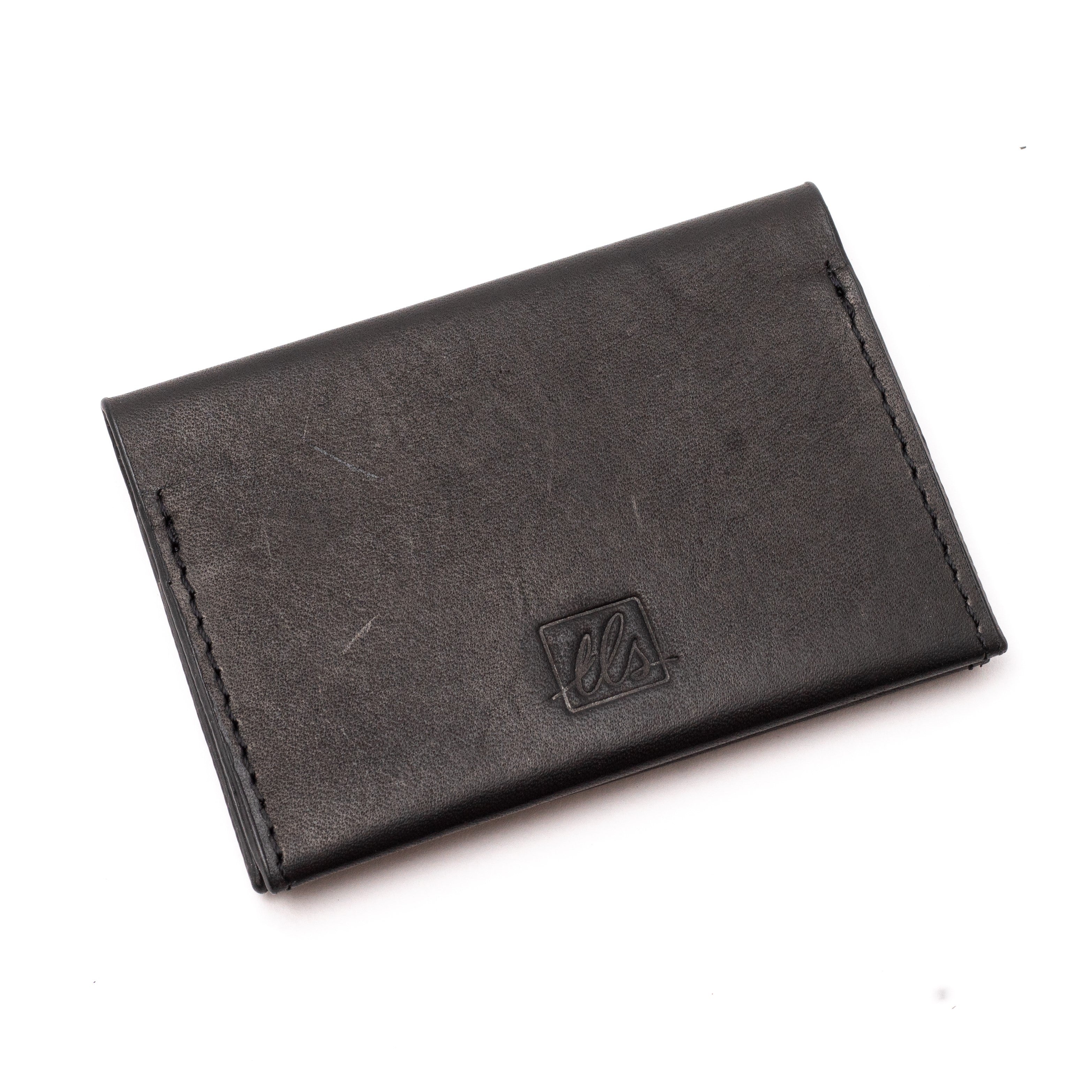 A closed black bi-fold credit card holder with visible stitching and a embossed logo on the front of the leather story
